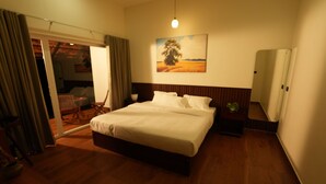 A bedroom with a large bed, a wooden floor, a painting on the wall, and a sliding door leading to a balcony. - Vaigayi Ayurvedic Resort (Kunnathunad)