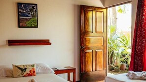 Une chambre d’hôtel avec deux lits, une porte en bois, un tableau et une vue sur l’extérieur.