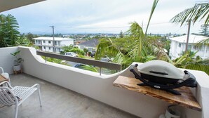 Un balcón con vista a una zona residencial, una silla blanca y un estante de madera con un casco y una sierra.