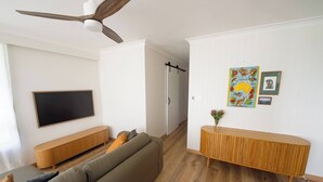Una sala de estar moderna con un televisor de pantalla plana, un sofá, una consola de madera y un ventilador de techo.