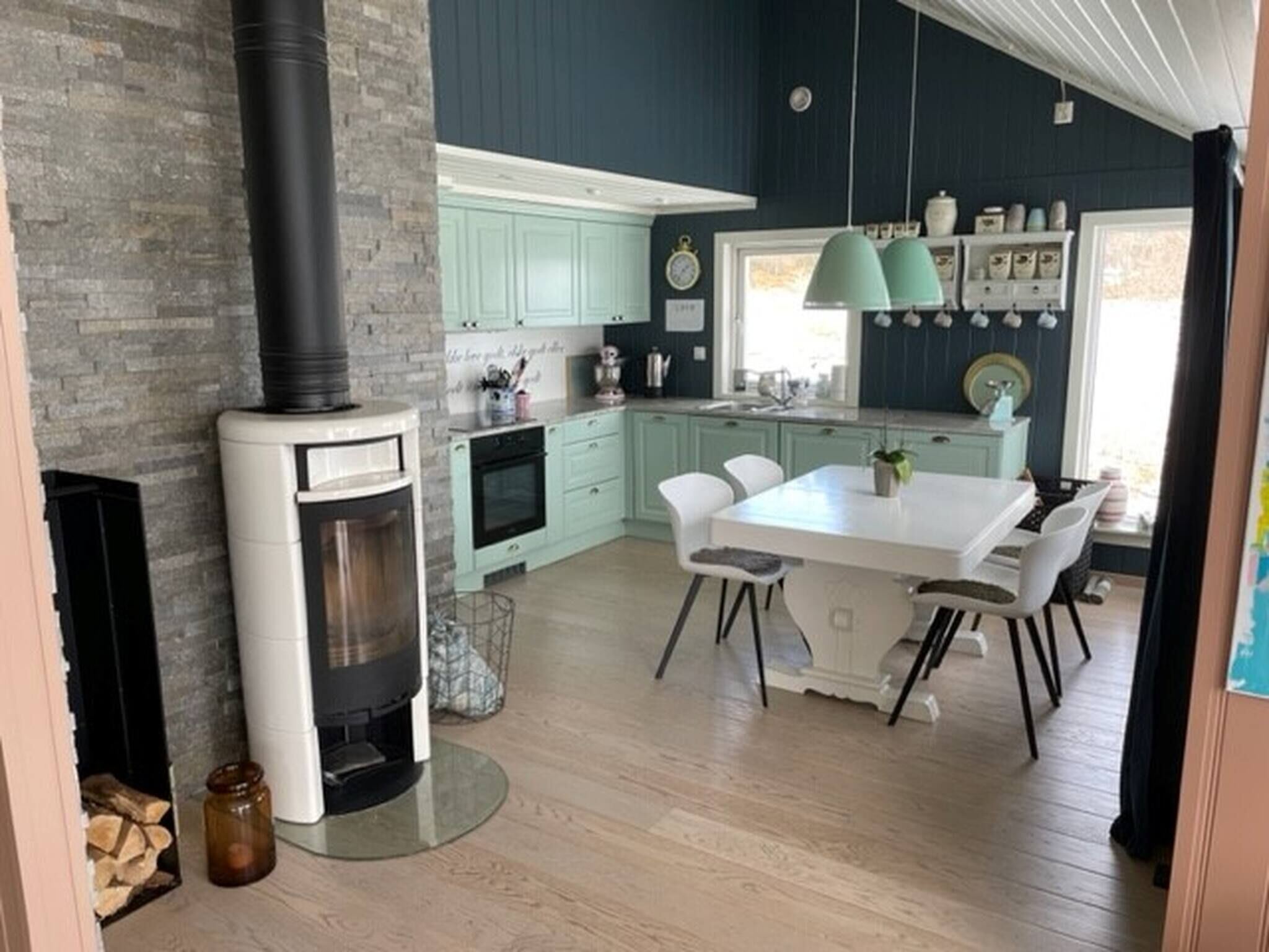 Een moderne keuken met blauwgroene kastjes, een witte eettafel en een zwart fornuis.