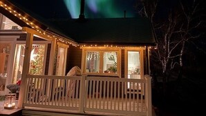 Een huis met een veranda en schoorsteen, onder een nachthemel met het noorderlicht.