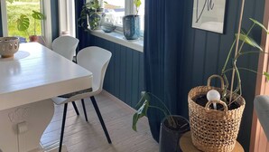 Een kamer met een witte tafel en stoelen, een raam met blauwe gordijnen en een tekstbord aan de muur.