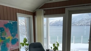 Een kamer met twee schommelstoelen, een groot raam met uitzicht op een besneeuwd landschap, en een kleurrijk abstract schilderij aan de muur.