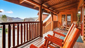 Een houten chalet met een veranda, houten stoelen en een trap naar de bovenverdieping.