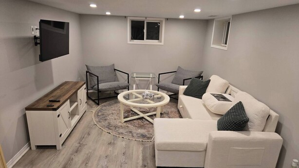 Ein modernes Wohnzimmer mit einer Couch, zwei Sesseln, einem Couchtisch und einem an der Wand befestigten Fernseher.