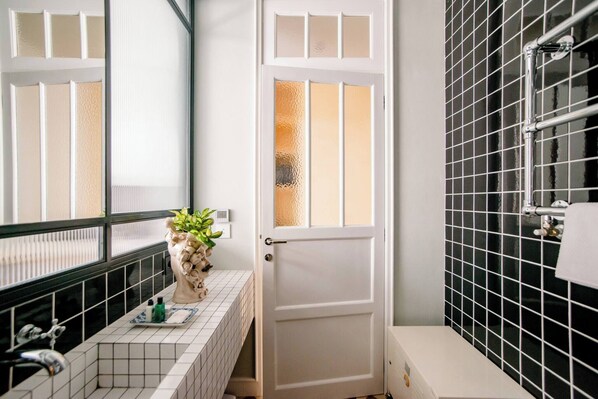 Un baño con puerta blanca, un lavabo con espejo, una planta en maceta y paredes cubiertas de baldosas negras.