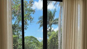 Ein modernes Wohnzimmer mit einem beigefarbenen Sofa, gemusterten Kissen und einem Glastisch. Durch ein großes Fenster sind ein Schwimmbad und Palmen zu sehen.