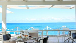 Un restaurant en bord de mer avec une terrasse, des parasols blancs et une vue sur l’océan.