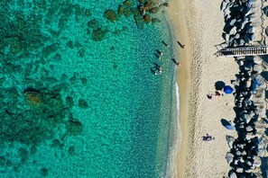 An aerial view of a beach with clear turquoise water, a sandy shore, and a pier with umbrellas. - Capo Vaticano Suites  (Ricadi)