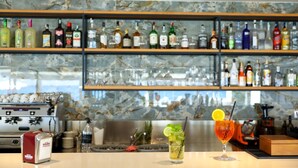 Un espace bar avec des étagères remplies de bouteilles d’alcool, une machine à café et un verre à cocktail orné d’une tranche de citron.