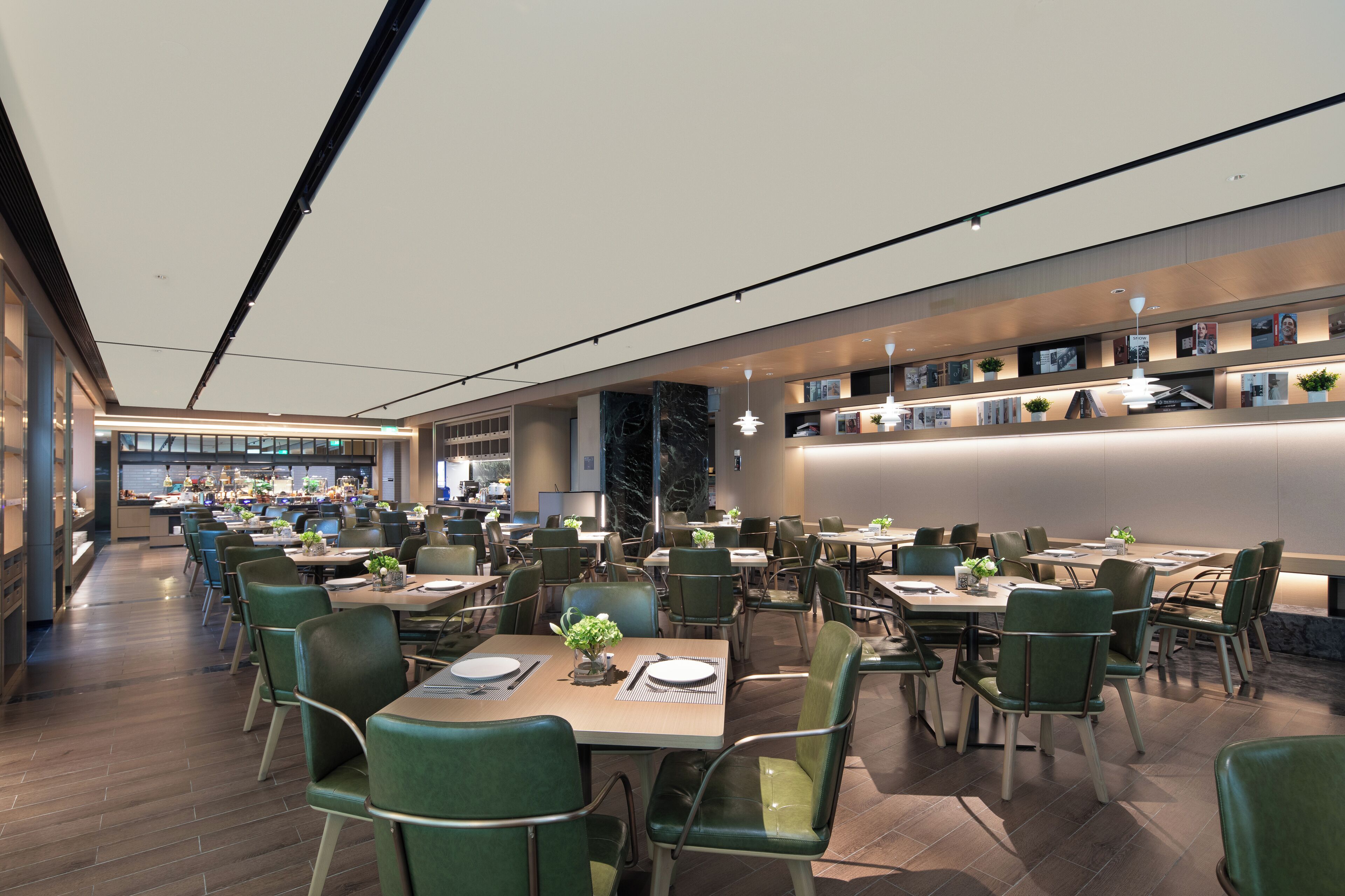 Een moderne eethoek met meerdere tafels en stoelen, een keuken op de achtergrond en een goed verlicht plafond.