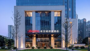 Een modern hotel met een opvallend “Hampton by Hilton” bord, grote glazen ramen en een goed verlichte ingang.