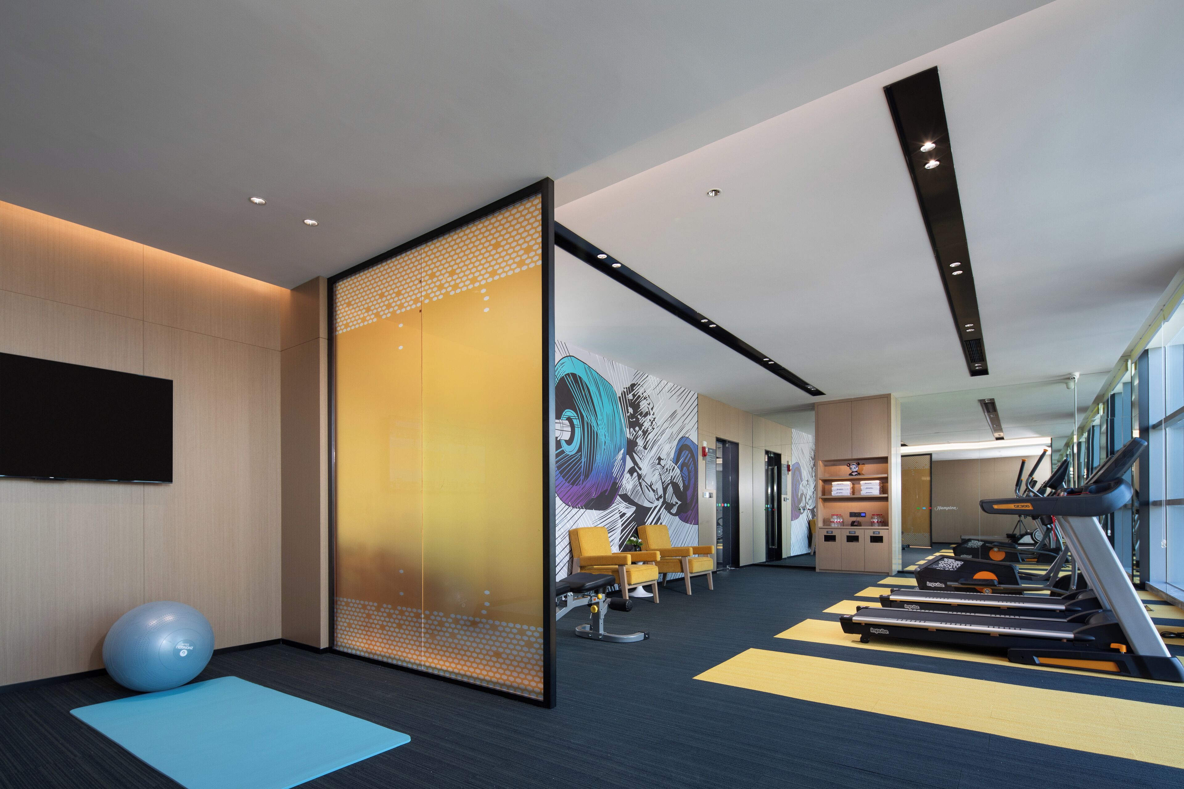 Una palestra moderna con attrezzature per esercizi, un tappetino blu e un muro decorato con un murale colorato.