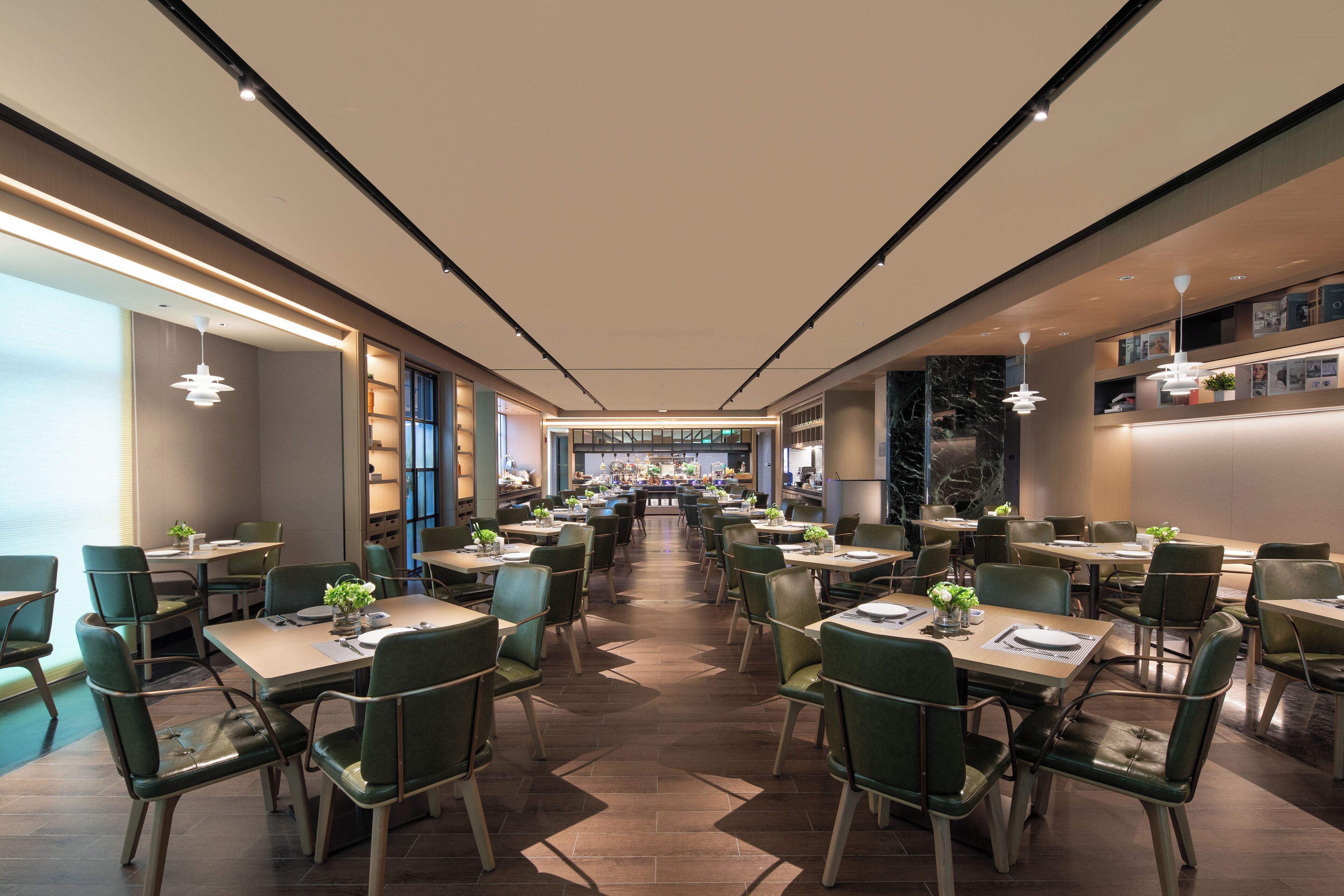 A modern dining area with multiple tables and chairs, a central bar, and a view of the kitchen in the background.