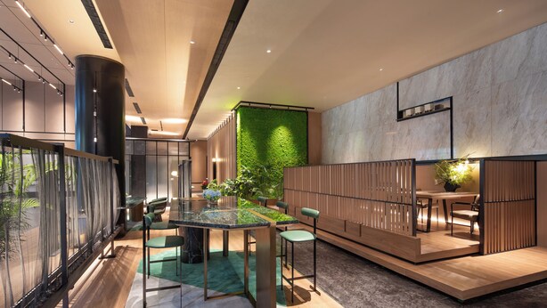 Een modern interieur met een eettafel met glazen blad, groene stoelen, een houten scheidingswand en een groene wand.