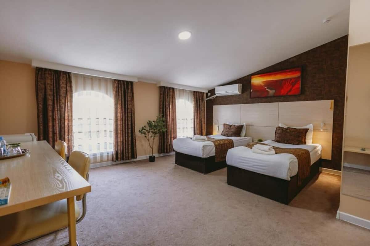 A hotel room with two beds, a dining table, and a large window with curtains.