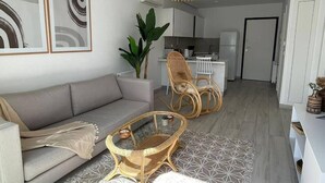 Ein modernes Wohnzimmer mit einem grauen Sofa, Korbstühlen, einem Glastisch und einem Teppich mit geometrischem Muster.