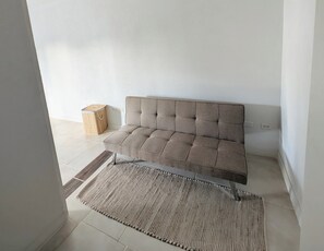 A neutral-toned sofa in a corner of a room with a light-colored floor and a woven rug. - The Cottages at Ocean Manor - Unit 2: Spacious 2BD 1BTH Townhouse with Seaview (Christ Church)