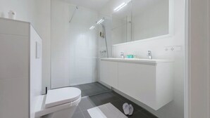 Ett modernt badrum med toalett, dusch och handfat, utrustat med en stor spegel och takbelysning.