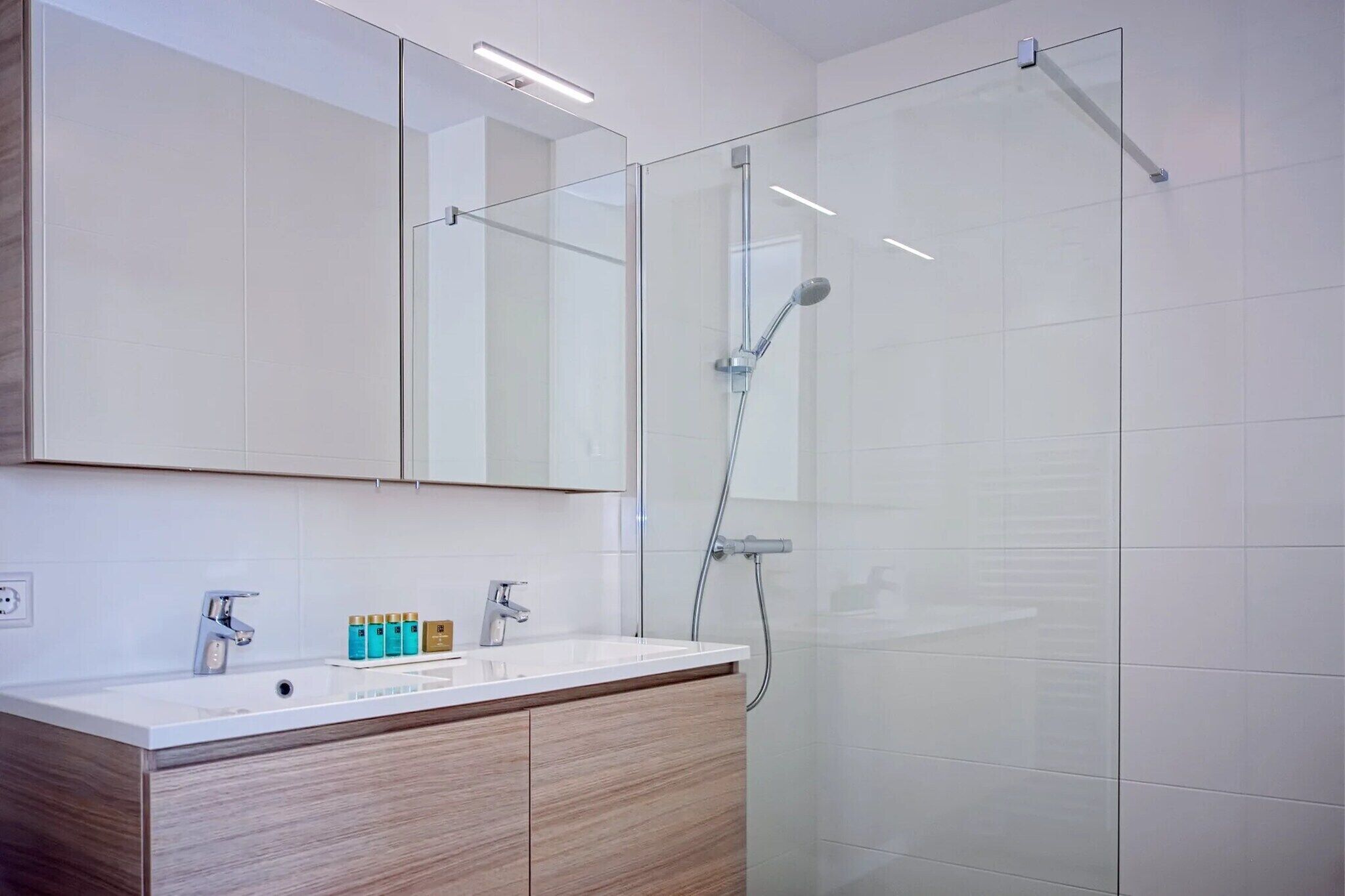 Ein modernes Badezimmer mit Duschkabine aus Glas, einem weißen Waschbecken mit Holzschrank und einem großen Spiegel darüber.