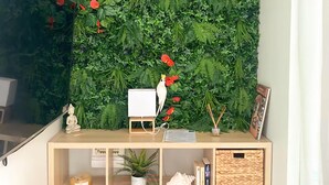 A room with a wall covered in green foliage and red flowers, a white desk with a small white bird figurine, and a wooden cabinet below. - Très beau gîte piscine - spa (Solliès-Pont)