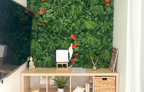A room with a wall covered in green foliage and red flowers, a white desk with a small white bird figurine, and a wooden cabinet below. - Très beau gîte piscine - spa (Solliès-Pont)