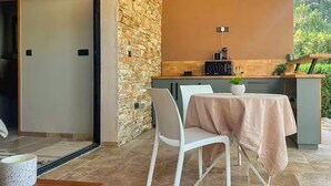 A patio area with a stone wall, a table with a tablecloth, and white chairs. - Très beau gîte piscine - spa (Solliès-Pont)