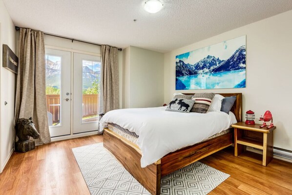 Ein Schlafzimmer mit einem hölzernen Bett, einem Nachttisch mit einer roten Lampe und einem Bergpanorama an der Wand.