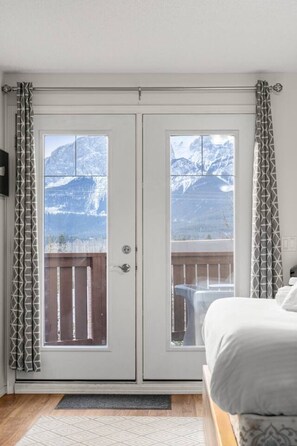 Habitación con dos puertas, vista a la montaña, una cama y una terraza de madera.