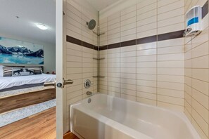 Ein Schlafzimmer mit einem Bett, Holzboden und einem Badezimmer mit Badewanne und gefliesten Wänden.