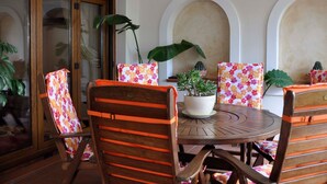 Uma área de refeições com uma mesa redonda, cadeiras de madeira com almofadas laranja e plantas em vasos.