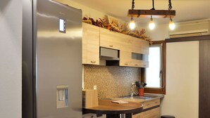 Uma cozinha compacta com geladeira de aço inoxidável, máquina de lavar embutida, armários de madeira, painel de azulejos e luminária pendente.