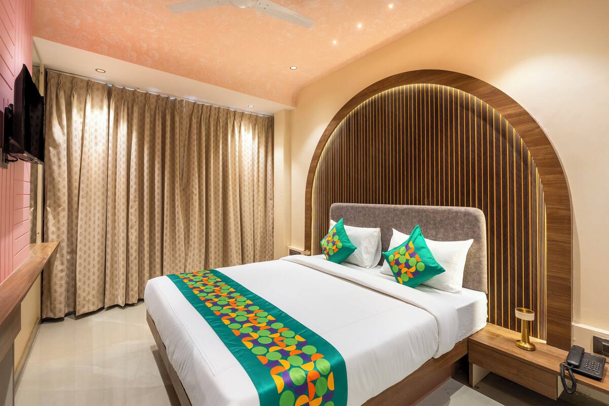 A hotel room with a bed, curtains, a TV, a bedside table with a lamp, and a phone.