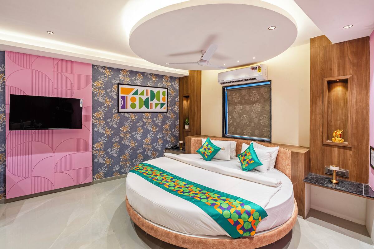 A modern hotel room with a round bed, a flat-screen TV, a ceiling fan, and a decorative wall panel.