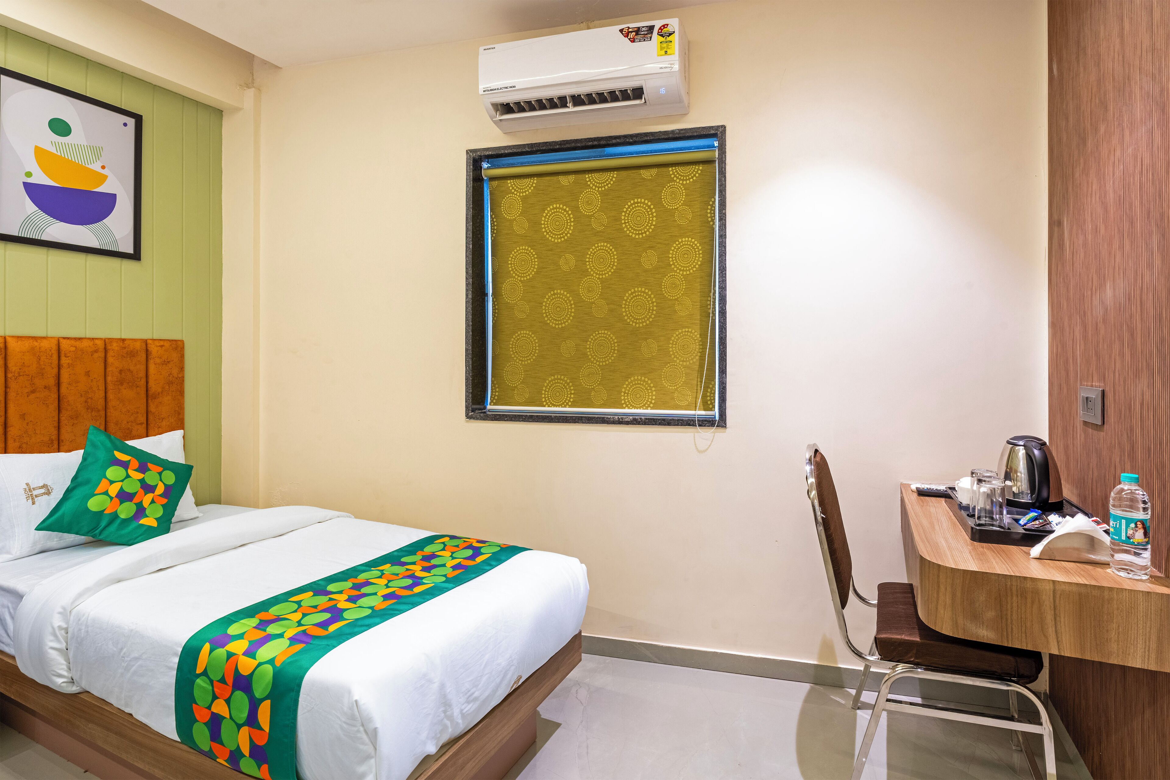 Une chambre d’hôtel équipée d’un lit, d’un bureau, d’une chaise, d’un climatiseur et d’une fenêtre avec un store à motifs.