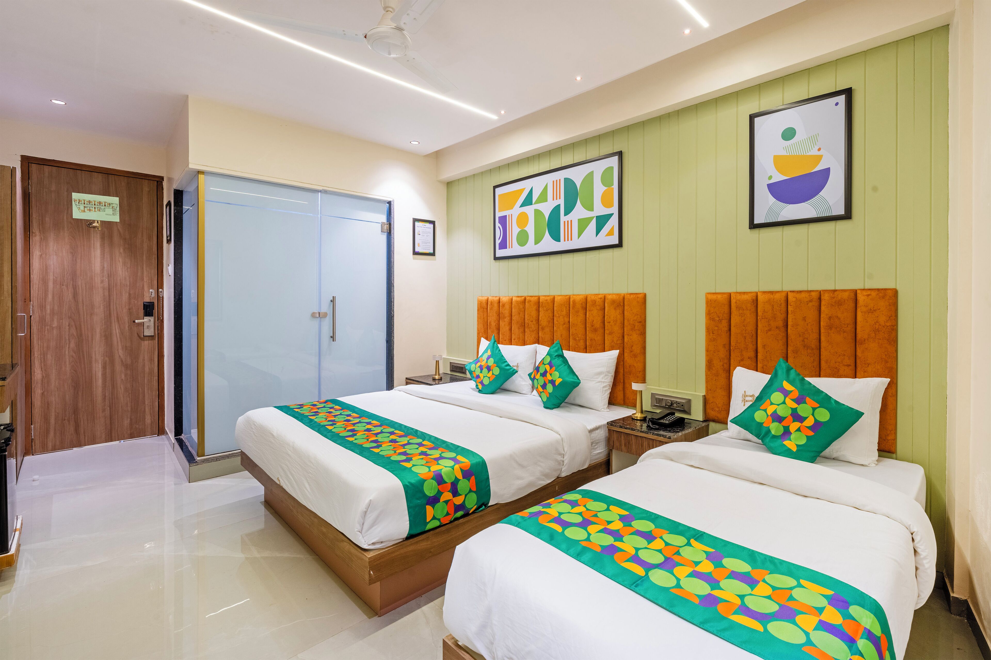 A hotel room with two beds, a wooden wardrobe, a door with a sign, and a framed abstract painting on the wall.
