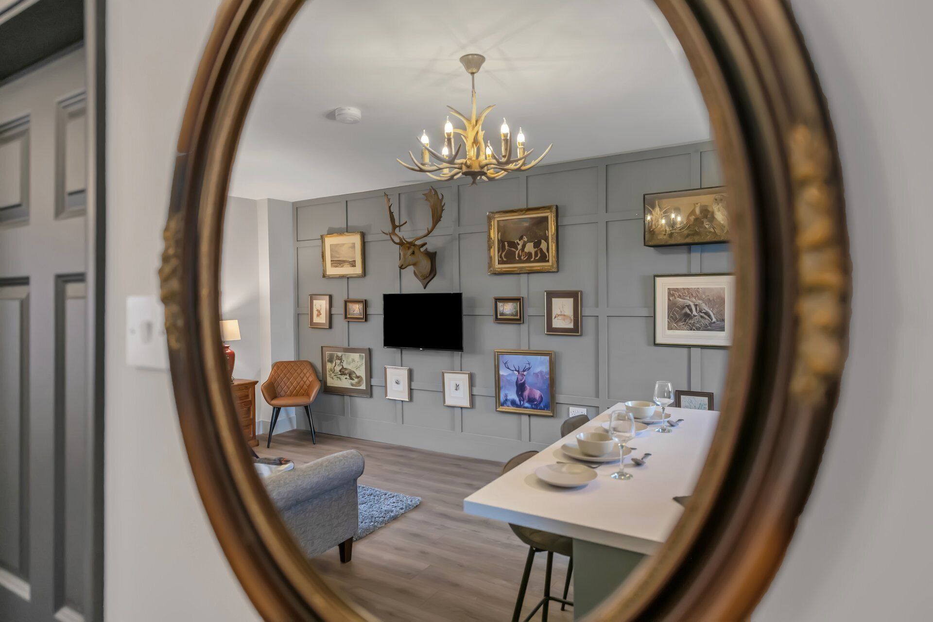 A dining area with a table set for four, a mounted deer head, and framed artwork on the wall.