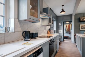 A modern kitchen with a white countertop, stainless steel appliances, and a view into the dining area. - Pools Cottage 1 Game Keepers Eco-Friendly Retreat (Kenilworth)