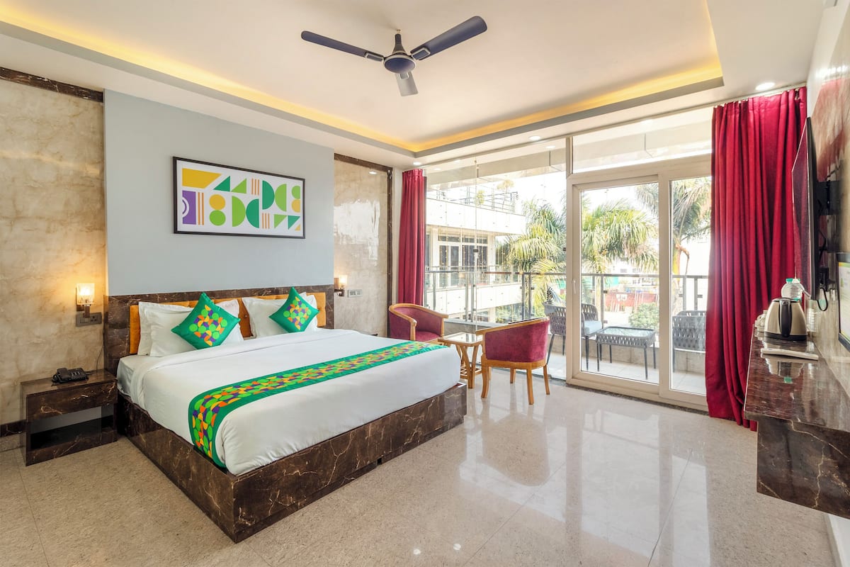 A hotel room with a large bed, a ceiling fan, a balcony with red curtains, and a view of the outside.