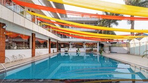 A swimming pool with a clear view of the surrounding area, including a multi-level building with balconies and a covered outdoor area. - Treebo Arya Palace With Swimming Pool (Shakti Enclave)