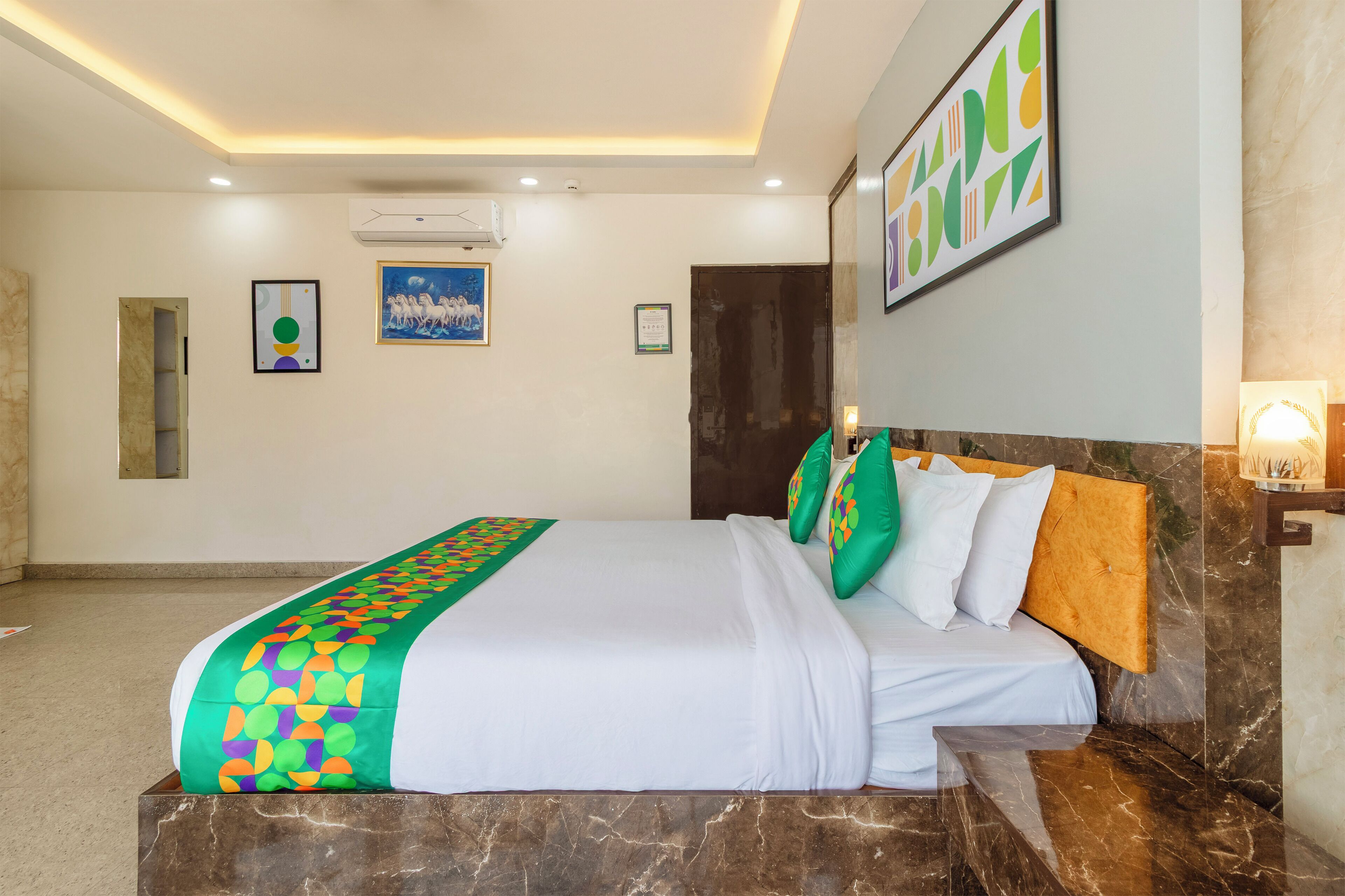 A hotel room with a bed, a headboard, a wall-mounted air conditioner, a framed picture, and a door.