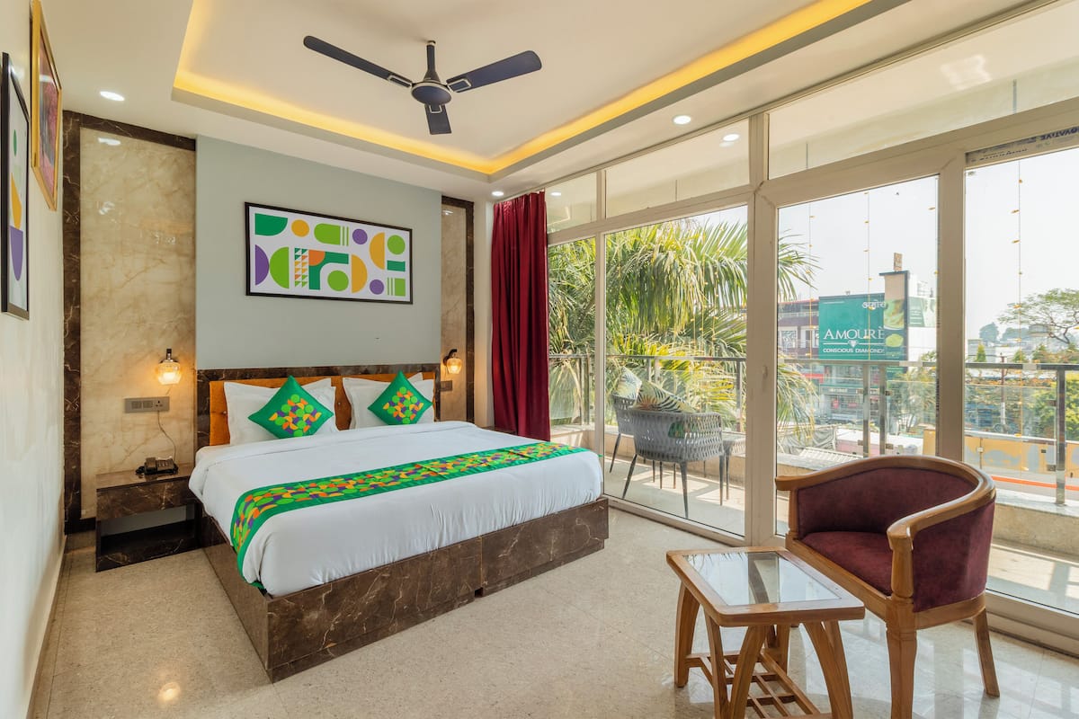 A hotel room with a large bed, a ceiling fan, a balcony with a chair, and a view of the city.