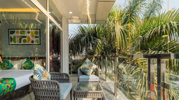 A balcony with wicker furniture, a glass table, and a bed with colorful pillows. - Treebo Arya Palace With Swimming Pool (Shakti Enclave)