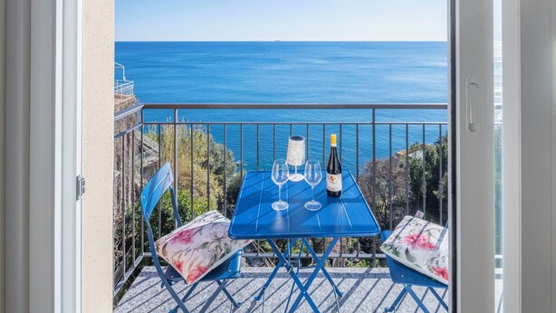 Een balkon met een tafeltje voor twee, met uitzicht op de kust.