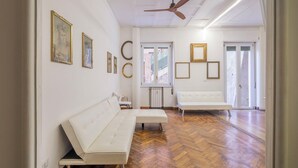 Una habitación amplia con suelo de parqué de madera, sofás blancos y un ventilador de techo.