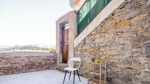 Un balcón con una silla blanca, un estante de madera y una pared de piedra.