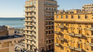 Un edificio de varios pisos con balcones, una calle en primer plano y una masa de agua al fondo.