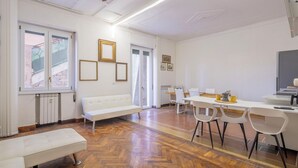Una habitación amplia con piso de madera en diseño espiga, muebles blancos y un comedor con sillas y una mesa.