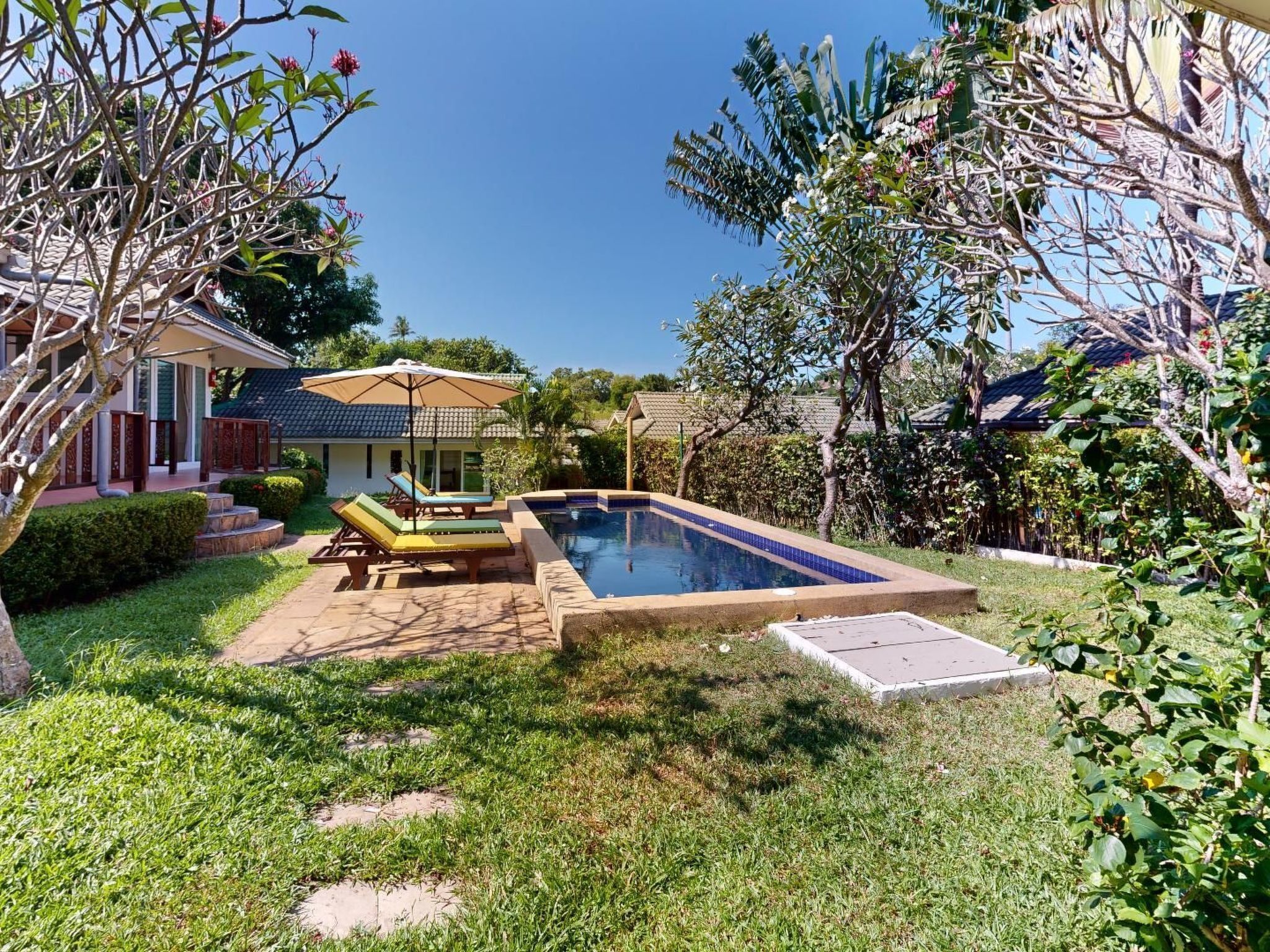 A backyard with a swimming pool, lounge chairs, and a covered seating area.